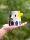 Person holding a cartoonish mug with a face against a blurred green background