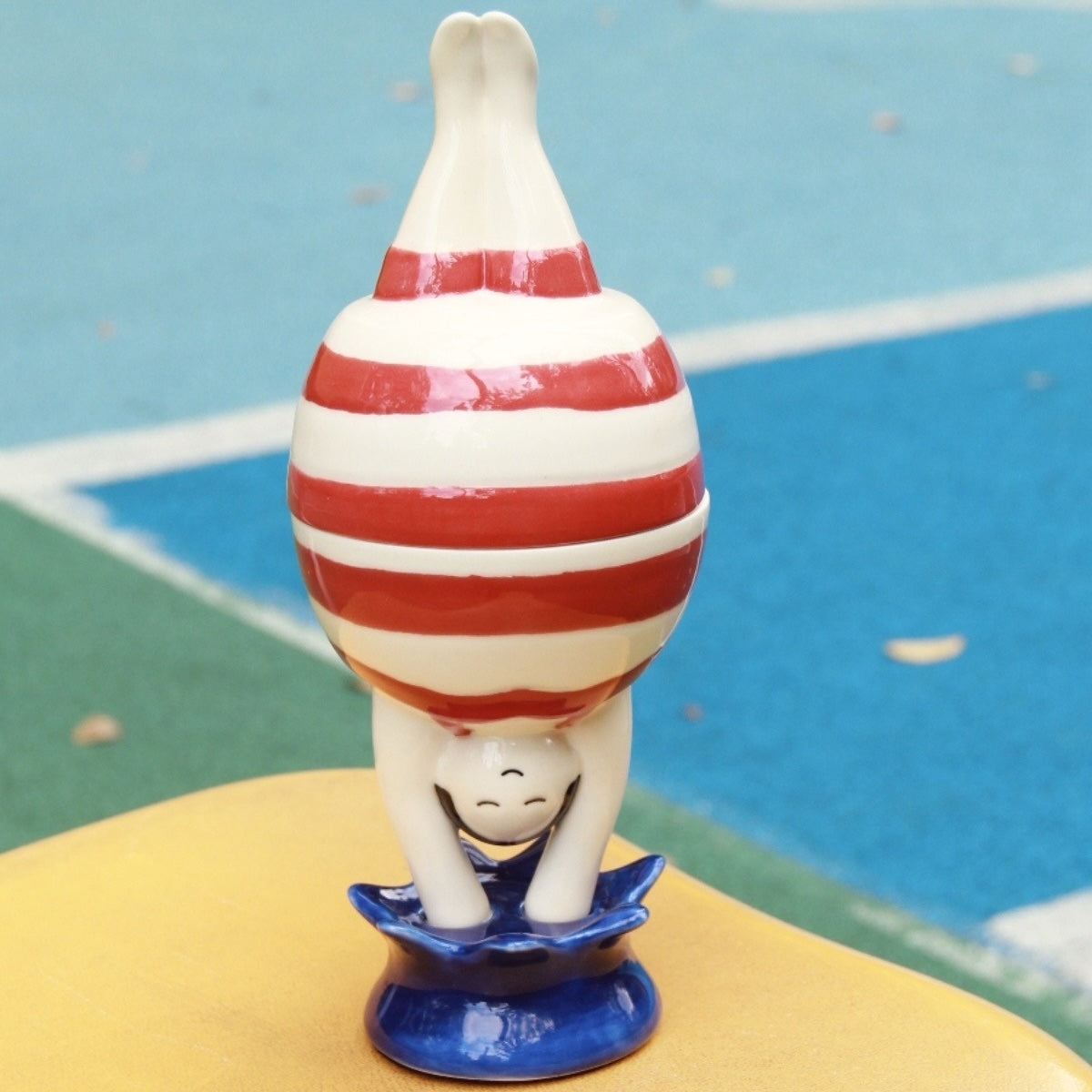 Whimsical ceramic candy jar mid-handstand, with a chubby striped belly
